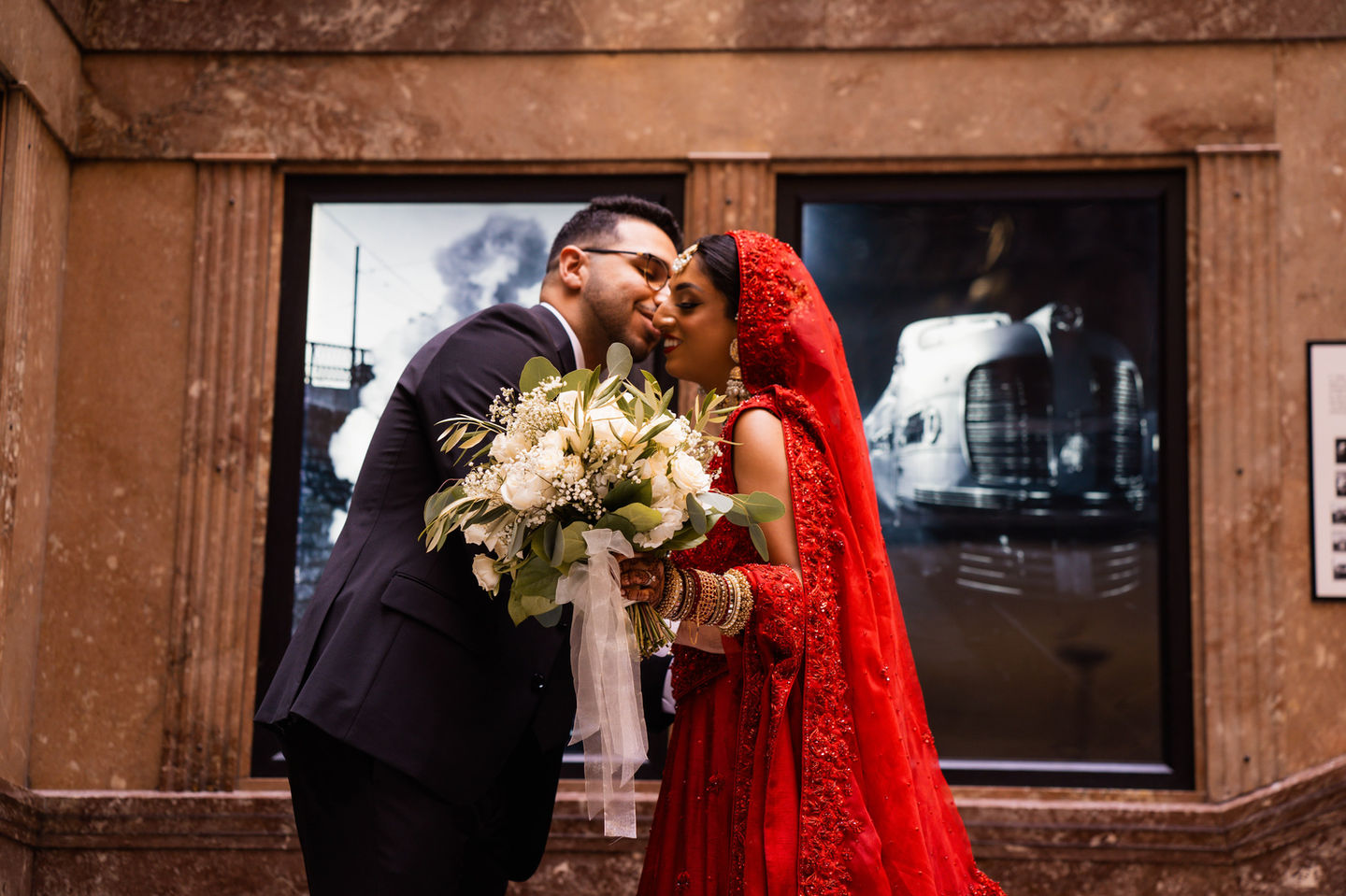 a bride in a red dress kisses her groom on the forehead