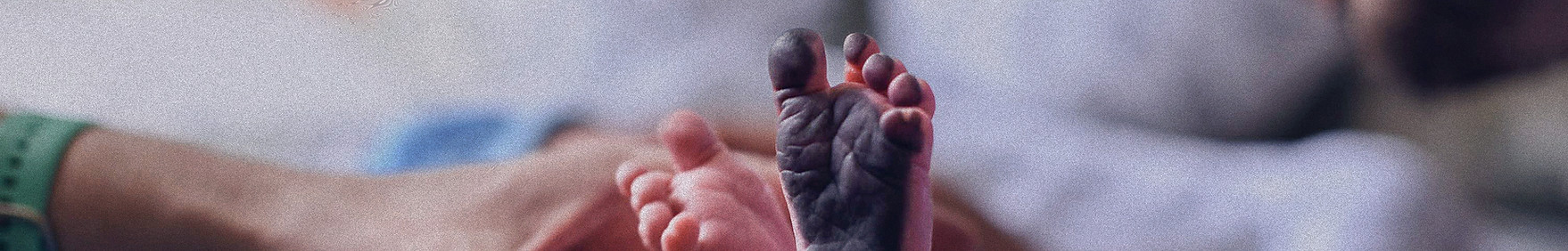 newborn feet, one foot has black ink on the pad of the foot in preparation for footprints