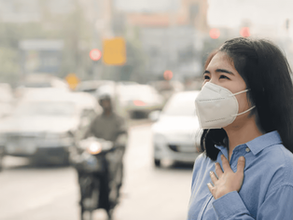 Perempuan menggunakan masker untuk melindungi diri dari polusi udara yang menurunkan kualitas udara di tengah lalu lintas padat.
