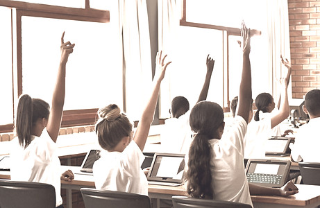 A group of students seated in a classroom raising their hands to actively participate in a learning experience