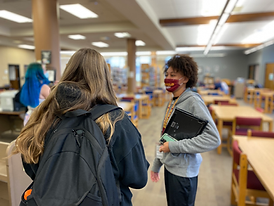 A staff member holding a binder talks to a student in a library