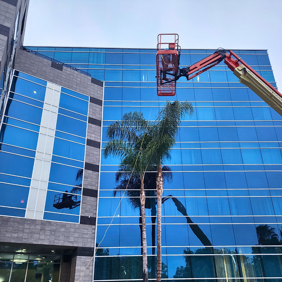 Loyal Exterior Cleaning worker in a lift to window clean beside a modern glass office building with a reflective blue facade.