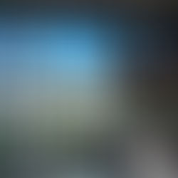 Two workers on a cherry picker clean large windows inside a modern glass building. Bright blue sky and greenery visible outside.