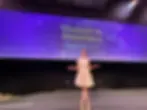 Amy Lillington in a white dress poses on stage with a purple backdrop reading "Women in Insurance Awards 2025," smiling under bright lights.