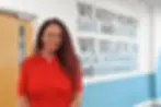 Nat Joyce standing and smiling for the camera, stood in the RiskSTOP Group office, in front of the Group's mission wording 'We keep people safe and secure. We believe in social responsibility and sustainability.'