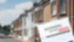 Row of brick houses under a blue sky, large insurance claim form stamped "REJECTED" in the foreground, conveying denial or setback.