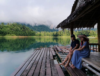 Guests relaxing on wooden deck overlooking Cheow Lan Lake and limestone mountains