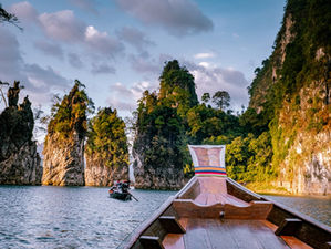 Long-tail boat cruising through Cheow Lan Lake surrounded by limestone cliffs in Khao Sok National Park, Thailand.