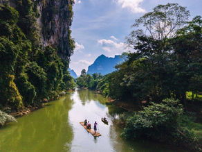 Travelers bamboo rafting along a peaceful river surrounded by tropical rainforest and limestone cliffs in Khao Sok, Thailand.