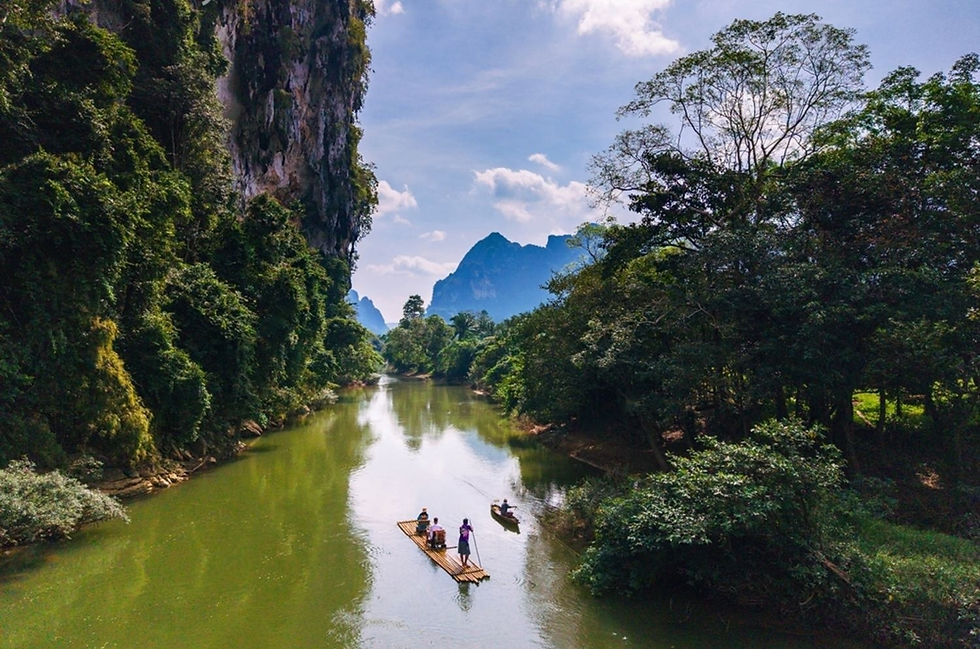 Travelers bamboo rafting along a peaceful river surrounded by tropical rainforest and limestone cliffs in Khao Sok, Thailand.
