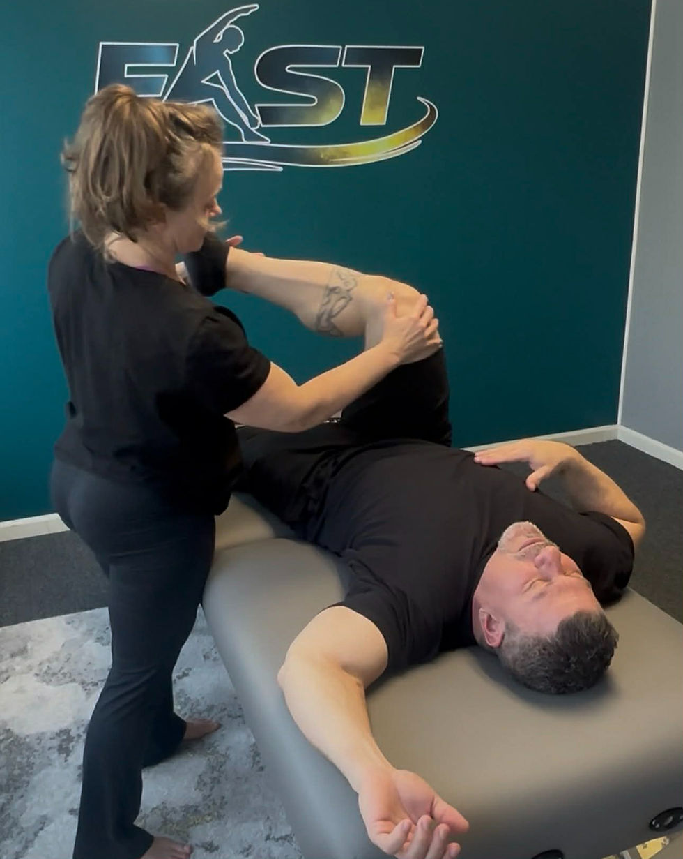 Eye-level view of a therapist gently stretching a client’s leg to release fascial tension