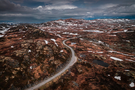 Einsame Straße durch die Landschaft der Hardangervidda in Norwegen. Schneefelder und dunkle Regenwolken am Himmel.

Hardangervidda, Norwegen, Skandinavien