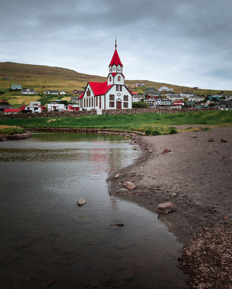 Kirche mit rotem Dach im Dorf von Sandavágur auf der Insel Vagar, Meer und Strand im Vordergrund.

Sandavágur, Vagar, Färöer Inseln