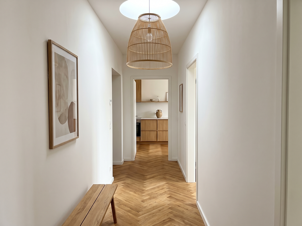Heller Flur mit Eichen-Fischgrätboden, weißen Wänden und einer Sitzbank aus Holz, der den Blick bis in die Küche am Ende führt.