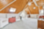 A spacious room with a vaulted ceiling featuring exposed wooden beams, creating an airy, rustic atmosphere.