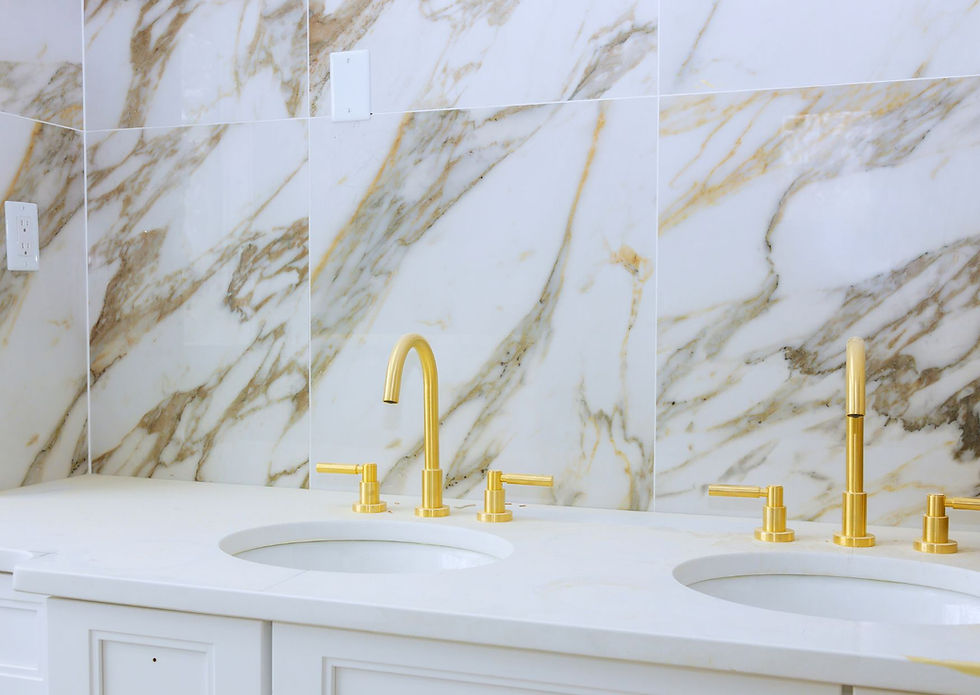 Luxurious double vanity with white and gold marble backsplash, undermount sinks, and brushed gold faucets.