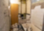 Completely gutted bathroom showing exposed walls, debris, and bathtub during major renovation demolition phase.