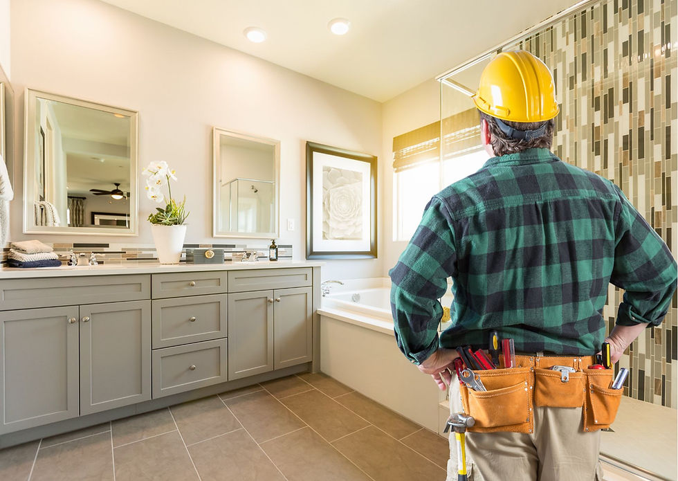Construction worker in yellow hard hat and tool belt examining finished bathroom with gray vanity and decorative tile.