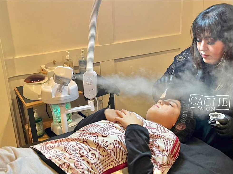 Esthetician at Caché Salon performing a professional facial treatment with steam on a client lying comfortably in the treatment room