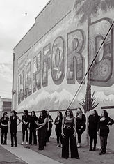 The Cache' Salon team lined up in front of the Greetings from Hanford mural, representing community pride.