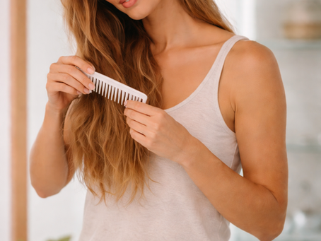 Woman gently detangling long hair with a wide-tooth comb before washing to prevent knots and breakage.