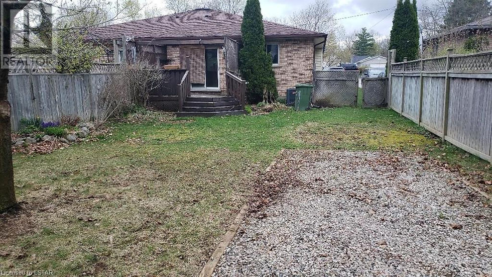 Old backyard deck before our outdoor renovation in a fenced backyard with a small brick house, deck steps, gravel area, and green lawn.