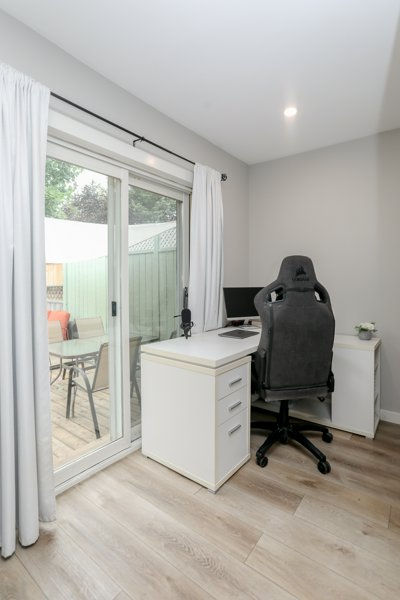 Bright home office with white desk, gray gaming chair, and sliding glass door opening to a patio sitting behind a new ensuite added during our primary bedroom renovation