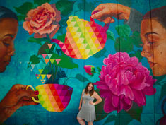 Woman poses in front of a vibrant mural featuring a colourful tea set and flowers representing fun content ideas in June.