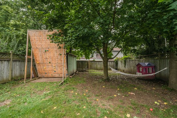 Backyard with a tree, outdoor climbing wall, hammock, and pink playhouse beside a wooden fence, calm and shaded showcasing the backyard after relocating the shed to create more usable space