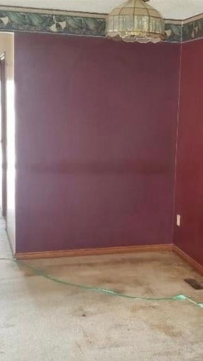 Empty room with deep purple walls, bare floor, and a hanging light fixture, giving a plain, unfinished feel. Dining room before adding navy accent wall during home renovation
