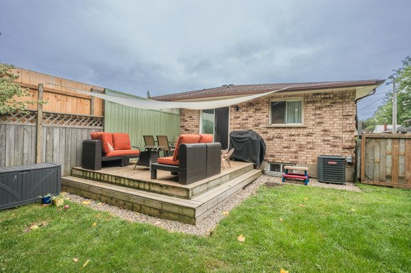 Backyard deck after rebuilding it for more functional outdoor space. Backyard patio with orange-cushioned chairs, grill, and table beside a brick house under a cloudy sky, calm suburban setting