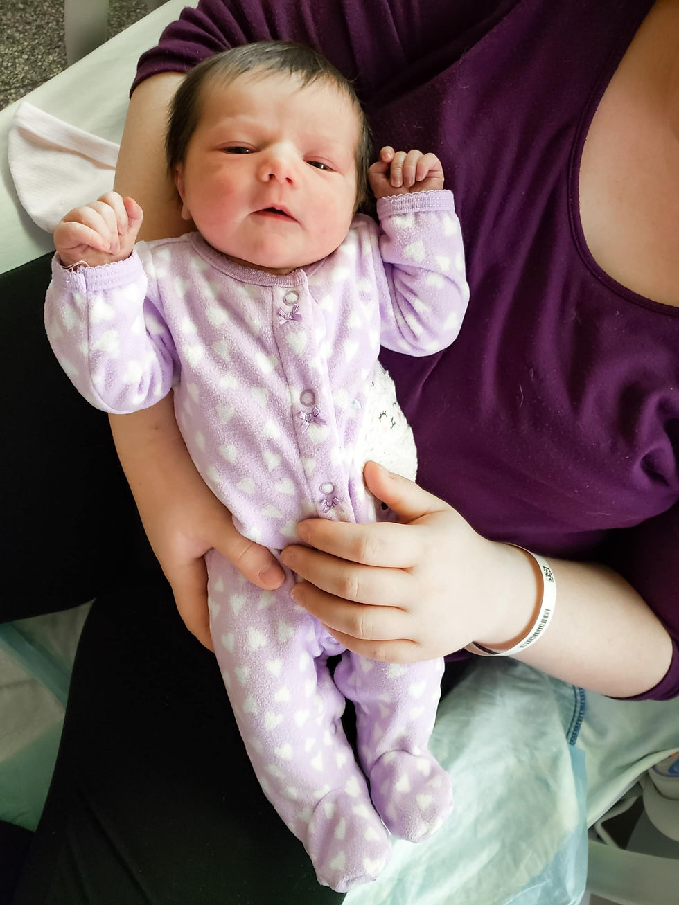 Newborn baby girl in a purple outfit, cradled in her mother's arms representing birth stories for induction births with epidurals.
