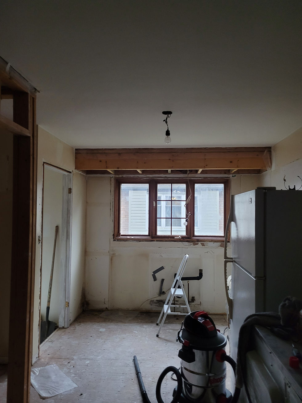 Unfinished kitchen under renovation with bare walls, exposed bulkhead beams, with a ladder, and tools by the window showing diy reno plans gone wrong.