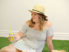 Woman in striped dress and straw hat sits on grass, holding a summer glass with a straw representing how to growyour business with sumemr marketing ideas.