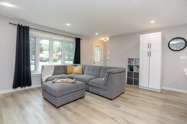 Open-concept living room after removing the non-load-bearing wall with grey sectional tastefully decorated in front of a large window.