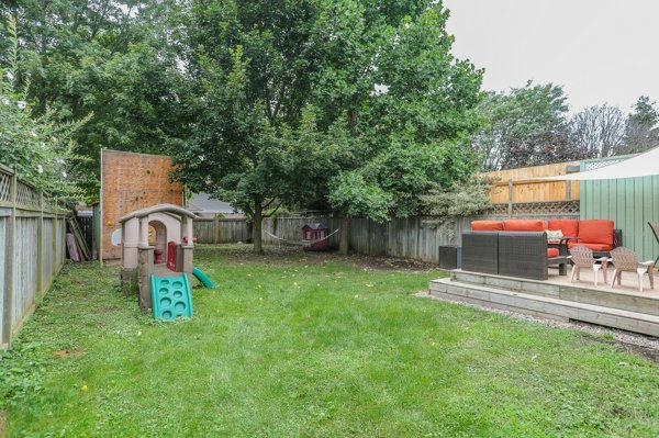 Finished backyard and landscaping after home renovation with green lawn, large tree, children’s playset, and patio seating on a deck beside a wooden fence.