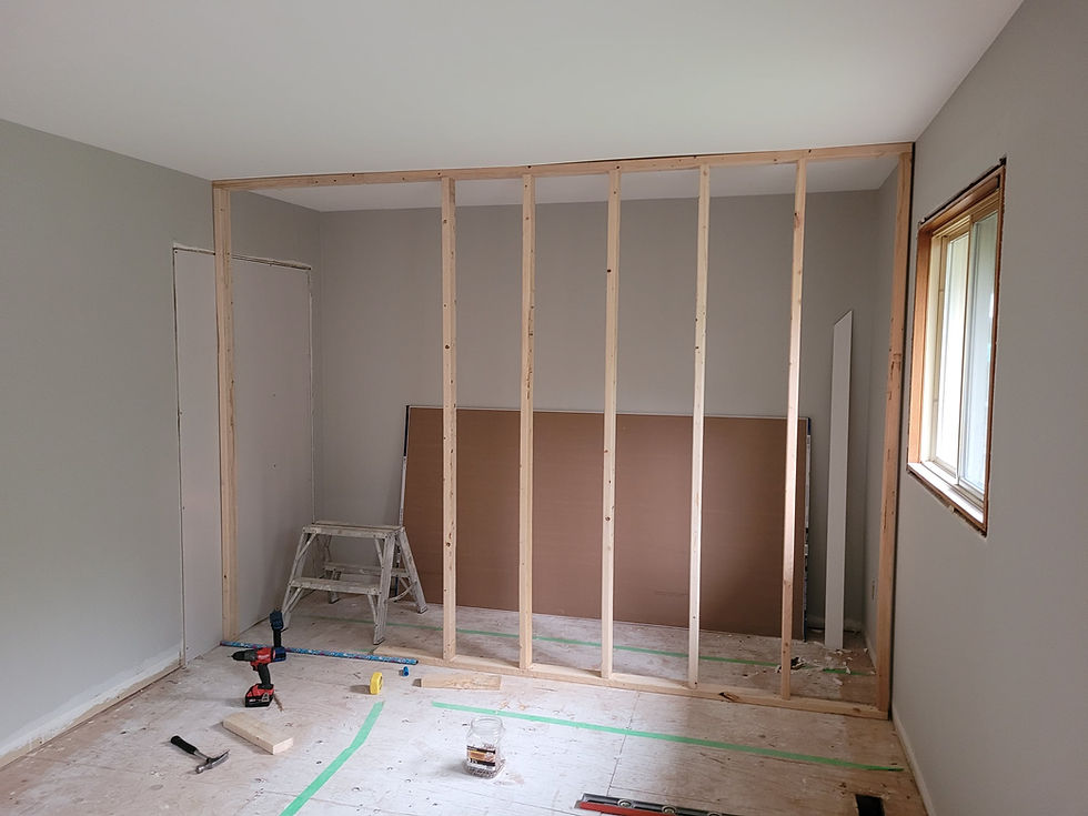 Partially renovated room with exposed wooden wall framing for a master walk in closet, tools on the floor, a step ladder, and a window letting in light.