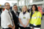 A small group of smiling airport security personnel.  Smiling towards the viewer, happy to help.