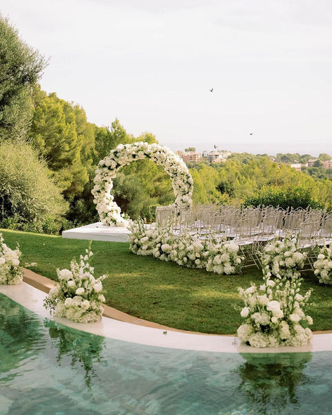 We adjusted the uneven railing with a platform to decorate this beautiful round wedding arch in front of a spectacular view of the sea in Mallorca. All flowers were kept in green and white with individual flower arrangements that framed the ceremony
