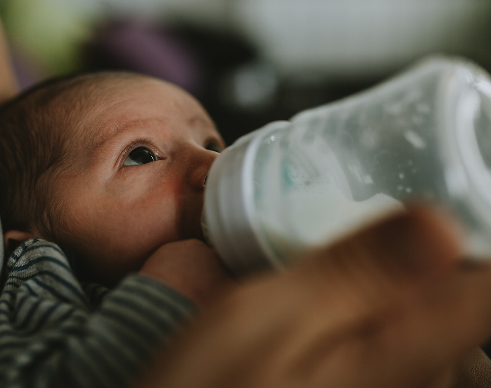 photo of a baby looking up and drinking milk from a bottle and
