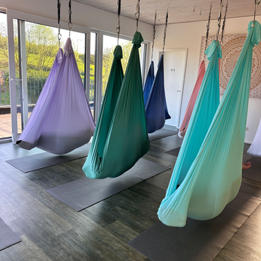 Schwangere Teilnehmerinnen liegen in der Seitlage - eingehüllt vom Aerial-Yoga-Tuch - 