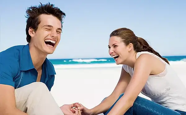Dette bildet viser en mann og kvinne som holder hender og ler satt på en strand