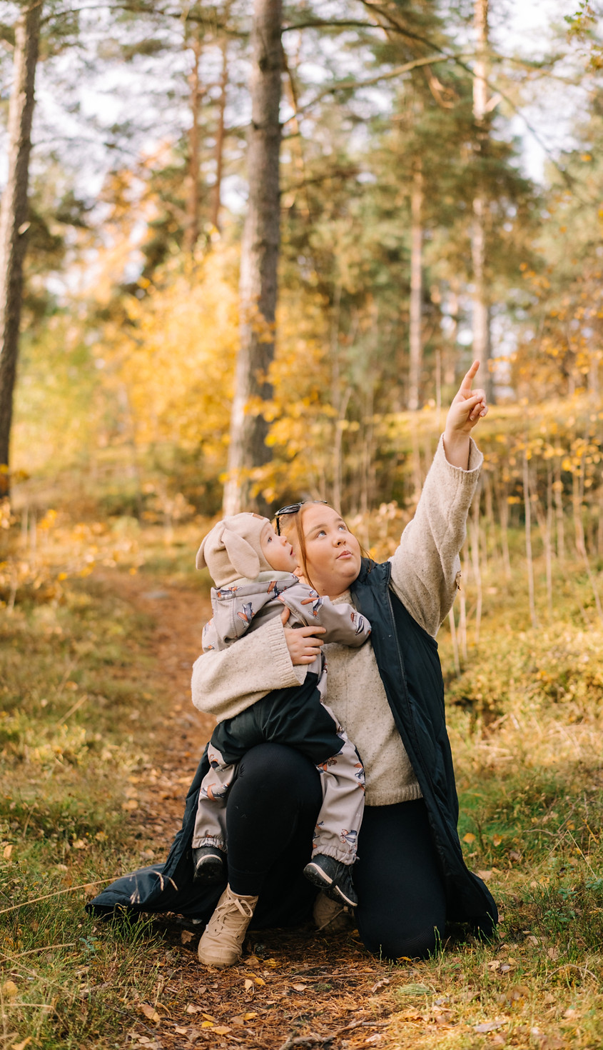 Hoivaaja kantaa lasta syksyisessä maisemassa