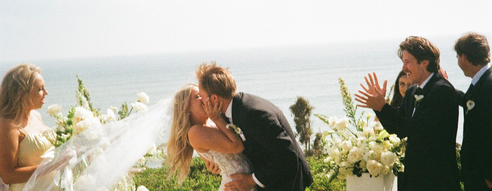 Bride and groom share a romantic dip and kiss as their guests applaud, all smiles on their wedding day.