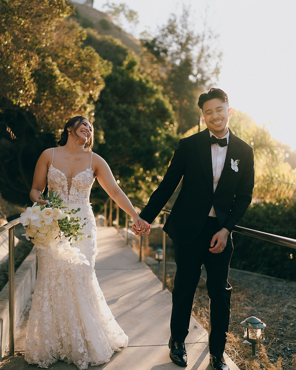 Bride and groom hand in  hand laughing with the sun beaming.