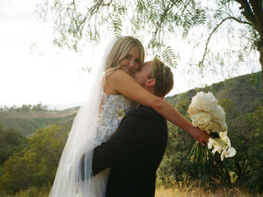 Bride smiles at the camera as the groom carries her in his arms, set against a scenic mountain and sky backdrop on their wedding day.