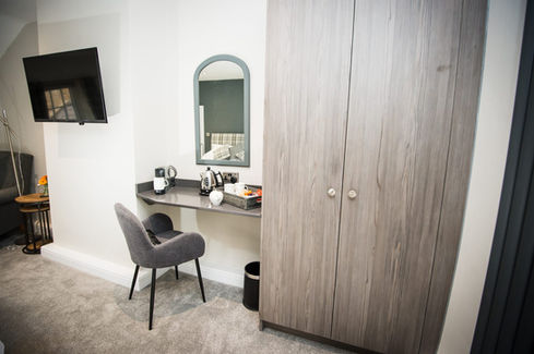 Bedroom with wardrobe, desk, chair, mirror, and television on the wall.