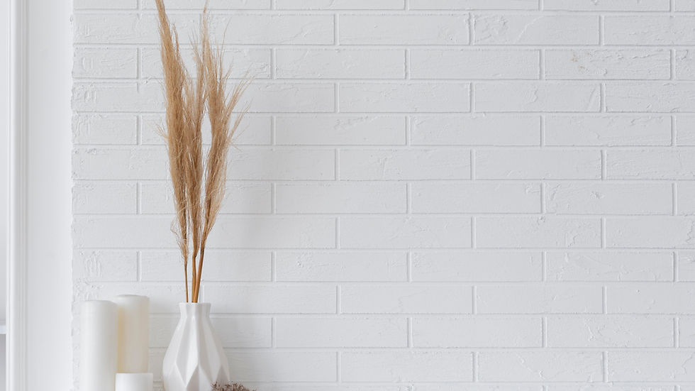 White vase with tall pampas grass on a shelf against a white brick wall. Two white candles beside it, creating a minimalist, calm ambiance.