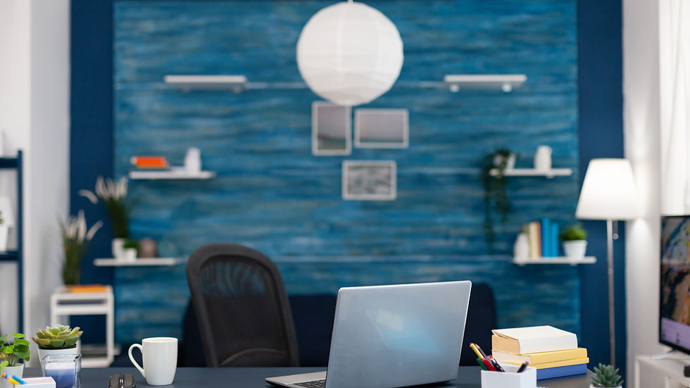 Office with a laptop, books, and a mug on a desk. Blue accent wall, white lamp, and shelves with plants and books create a calm vibe.
