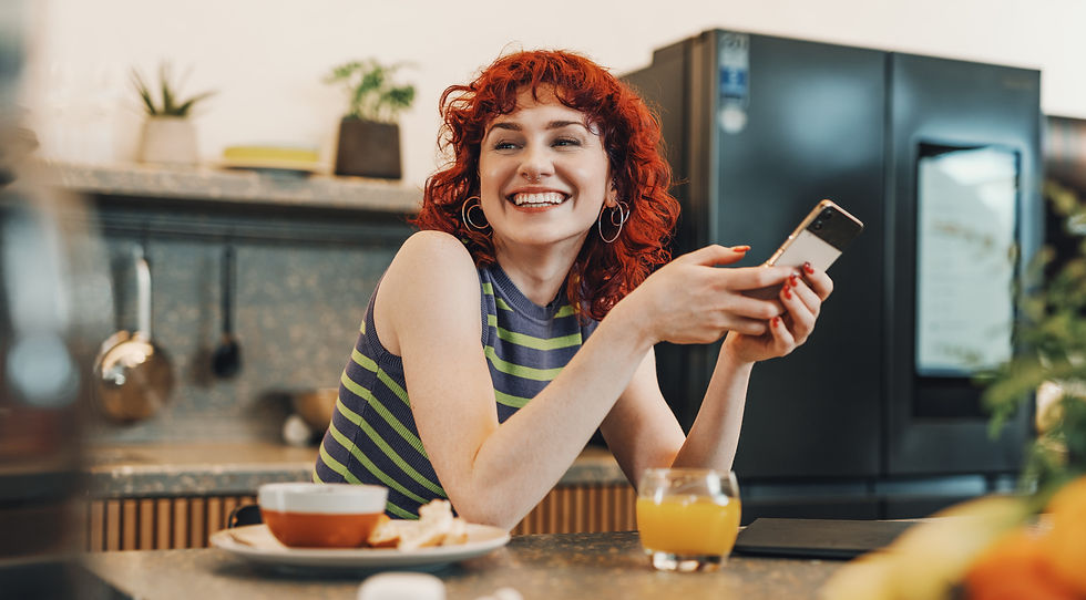 A young woman sits at her kitchen counter, happy about the discount notification she received on her cell phone.